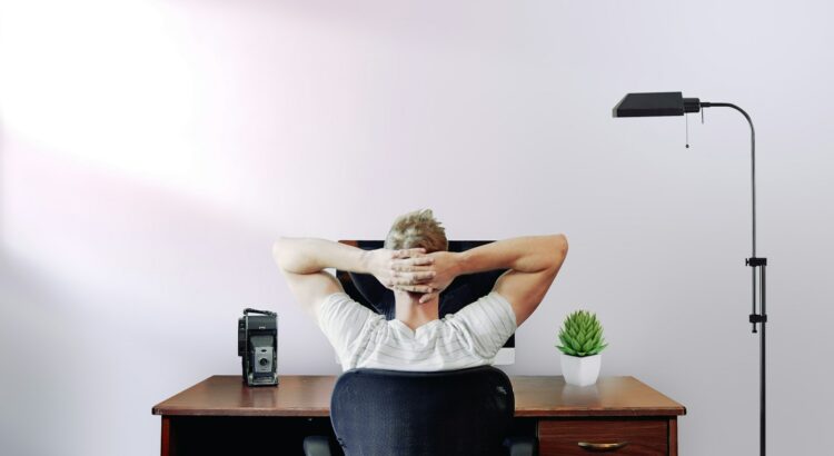 man holding his head while sitting on chair near computer desk