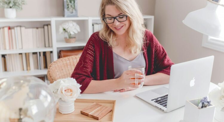 woman smiling holding glass mug sitting beside table with MacBook